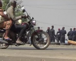 A still image from video thay shows people riding past on a motorbike looking at soldiers standing at a checkpoint in Bouake